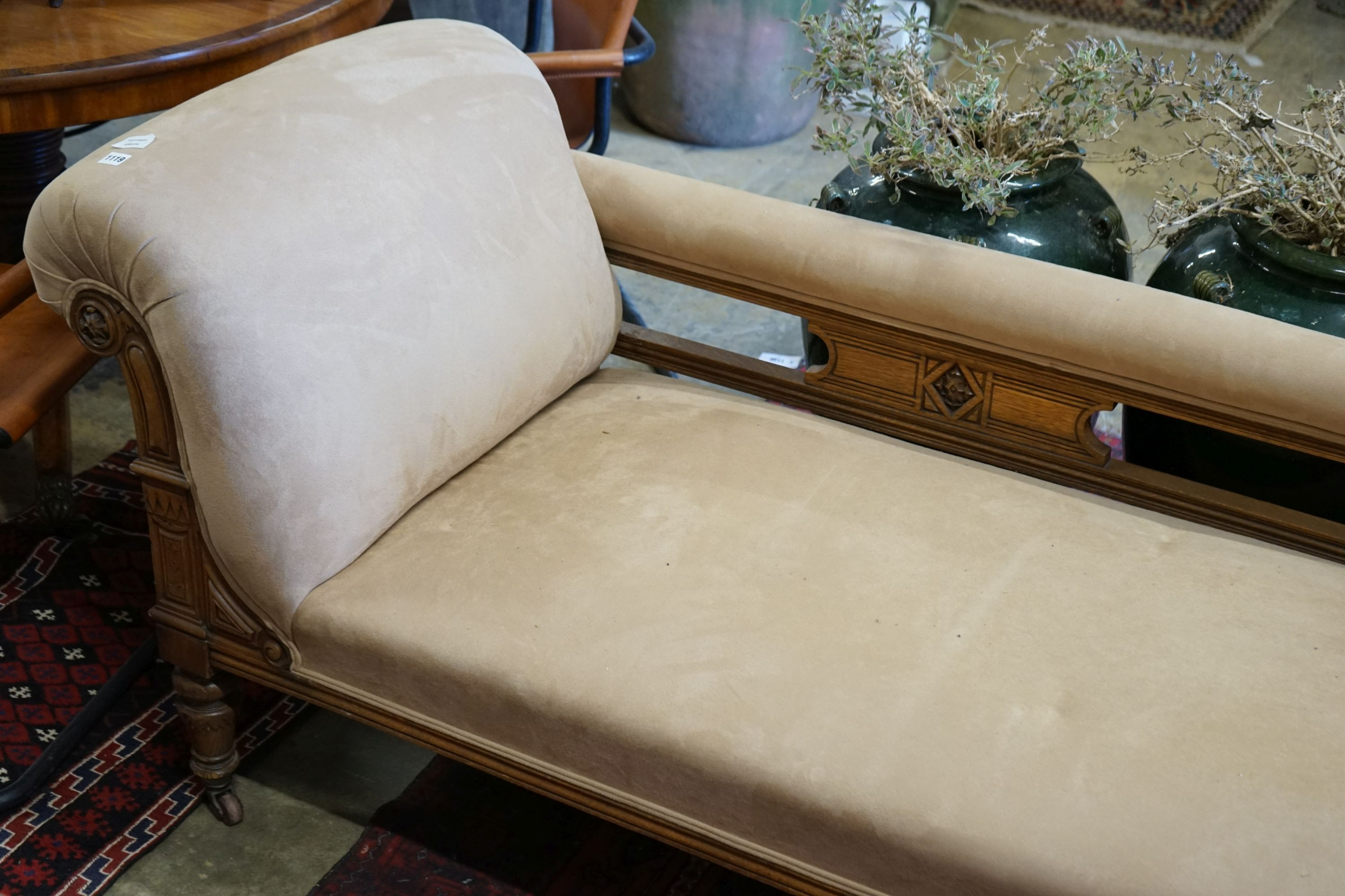 A late Victorian carved oak chaise longue upholstered in fawn suede, length 180cm, depth 70cm, height 79cm